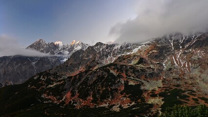 Panoramic photo of the rocky peaks of the High Tatras at sunrise with the first layer of snow in early autumn