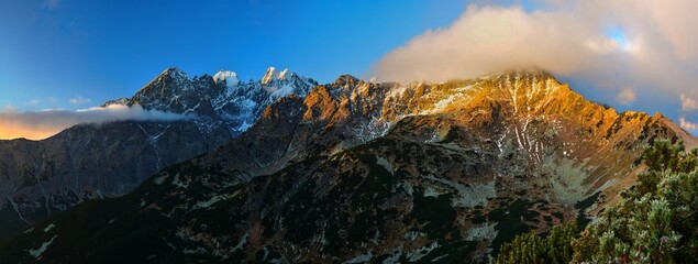 Panoramic photo of the rocky peaks of the High Tatras at sunrise with the first layer of snow in...