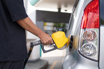 Closeup image of hand holding nozzle fuel fill oil into car tank at gas station.