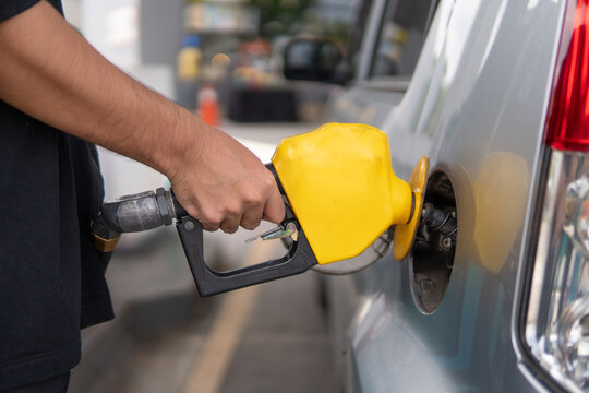 Closeup image of hand holding nozzle fuel fill oil into car tank at gas station.