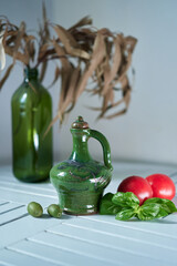 Green ceramic bottle of olive oil and tomatoes with leaves basil on the white kitchen table. Italian traditional food , ingredient, recipes. High quality photo