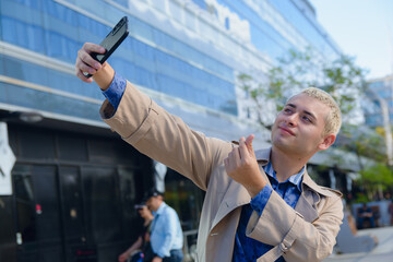 Handsome blond freelance young man in formal clothes taking selfie photo with his phone outdoors