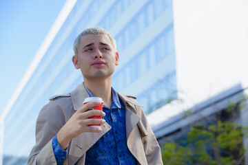 elegant blond young latin man, distracted outdoors drinking coffee and looking around