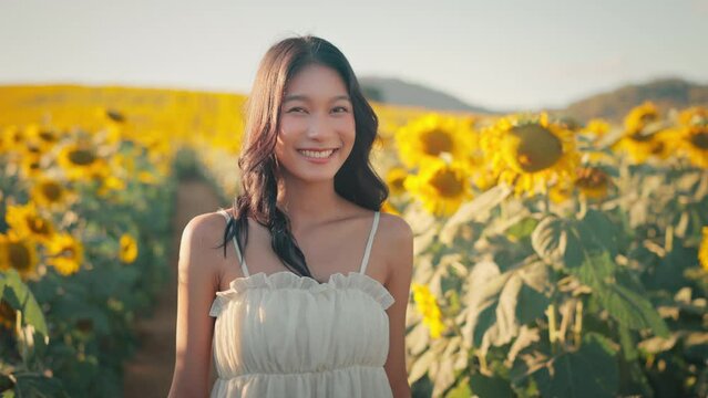 Happy asian woman smiling in sunflower field outdoors, Cheerful Young female looking at the camera feeling free in blooming garden in summer day.