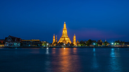 Wat Arun stupa, a significant landmark of Bangkok, Thailand, stands prominently along the Chao Phraya River, with a beautiful night sky.