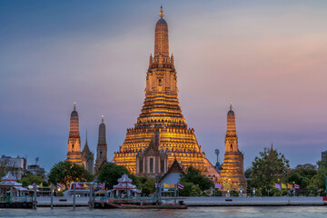 Fototapeta premium Wat Arun stupa, a significant landmark of Bangkok, Thailand, stands prominently along the Chao Phraya River, with a beautiful sunset sky.