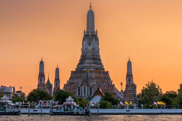 Wat Arun stupa, a significant landmark of Bangkok, Thailand, stands prominently along the Chao Phraya River, with a beautiful sunset sky. - 785191514