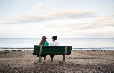 Two women sitting on the bench on the beach, chatting and enjoying the scenery. Milford Beach. Auckland.