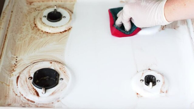 Cleaning gas stove with pink sponge and detergent. Woman is wearing white gloves. Washing kitchen surfaces