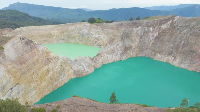 Kelimutu volcano crater on Flores. Two large bodies of water, one of which is green. The other is blue. The scene is serene and peaceful, with the water reflecting the surrounding landscape.