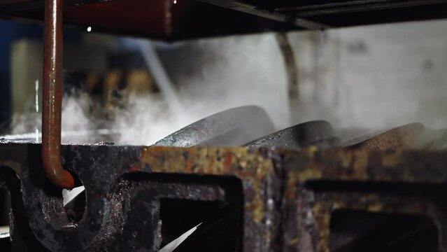 Steam rises from freshly quenched metal parts in a casting foundry's cooling station
