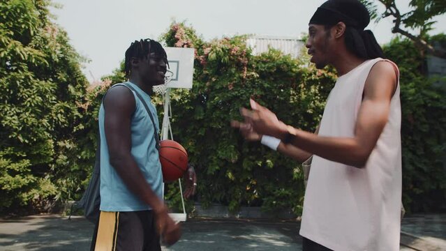 Low angle of two African American sportsmen greeting each other at streetball playground outdoors