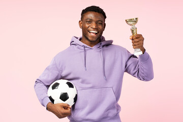 Portrait of African American athlete celebrating victory, holding a gold cup and soccer ball