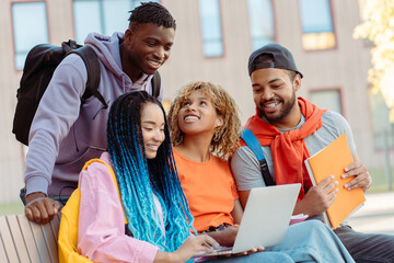 Group of young African American students sitting in park near college, holding laptop, meeting