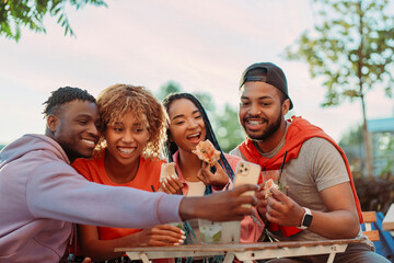 Group of smiling stylish African American friends taking selfie, eating pizza, drinking lemonade
