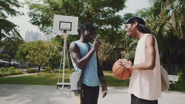 Wide shot of two black men chatting while meeting before game on streetball playground