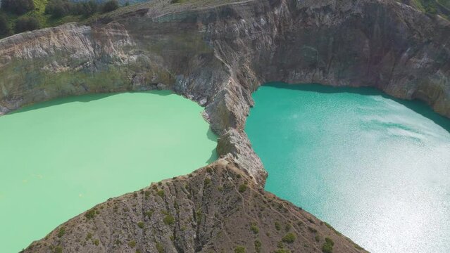Kelimutu volcano crater on Flores. Two large bodies of water, one of which is green. The other is blue. The scene is serene and peaceful, with the water reflecting the surrounding landscape.