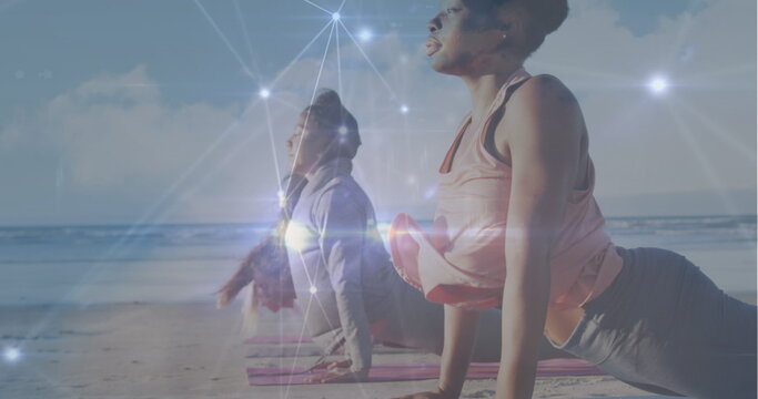Image of network of connections over diverse women practicing yoga at beach