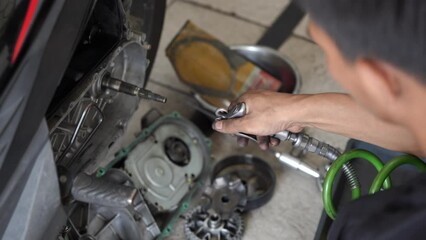 Mechanic cleans motorcycle engine with air blow gun. Mechanic works in motorcycle repair shop. Concept of repair and maintenance service
