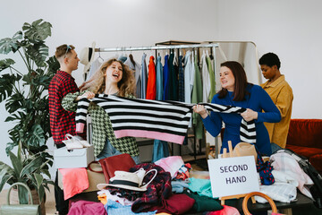 young people in second hand shops, choice of clothes, the possibility of a second life for clothes, woman take away each other's clothes, having fun - obrazy, fototapety, plakaty