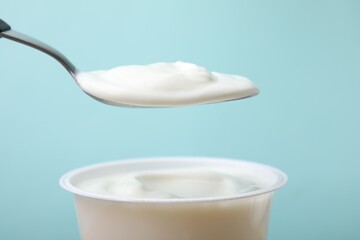 Eating delicious natural yogurt on light blue background, closeup