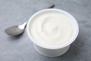 Delicious natural yogurt in plastic cup and spoon on grey table, closeup