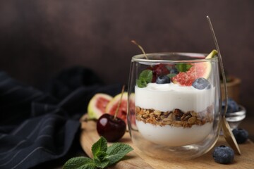 Glass with yogurt, berries, mint and granola on wooden table. Space for text