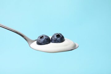 Spoon with yogurt and blueberries on light blue background, closeup