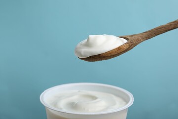 Eating delicious natural yogurt on light blue background