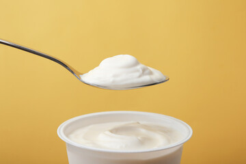 Eating delicious natural yogurt on yellow background