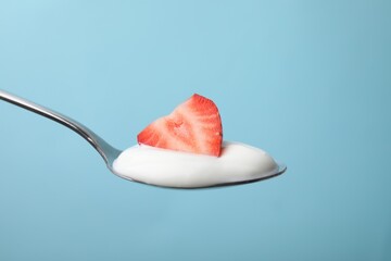 Delicious natural yogurt with fresh strawberry in spoon on light blue background