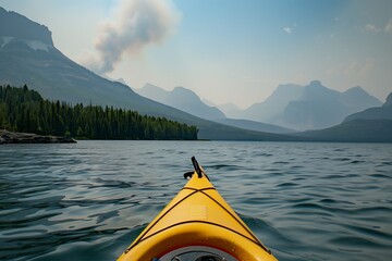 A closeup shot of the front tip of an open yellow kayak on calm waters, with mountains in misty background, smoke from forest fires creating hazy atmosphere, stunning natural color - obrazy, fototapety, plakaty