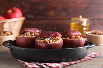 Tasty baked apples with nuts in baking dish on wooden table, closeup