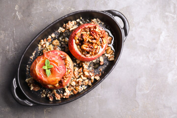 Tasty baked apples with nuts, honey and mint in baking dish on gray textured table, top view. Space for text