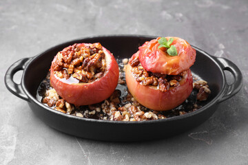 Tasty baked apples with nuts, honey and mint in baking dish on gray textured table