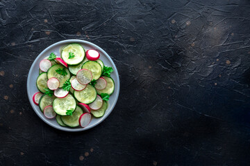 Fresh cucumber and radish salad with parsley, overhead flat lay shot. Simple vegan recipe on a slate background. Healthy diet, with a place for text