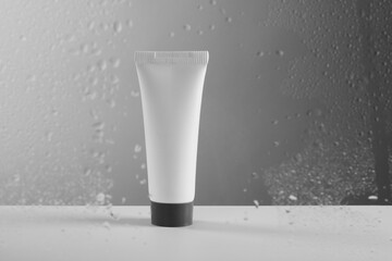 Tube with moisturizing cream on grey background, view through wet glass