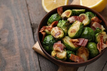 Delicious roasted Brussels sprouts and bacon in bowl on wooden table, closeup