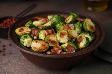 Delicious roasted Brussels sprouts and bacon in bowl on brown table, closeup