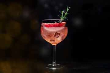 Fancy cocktail with fresh fruit. Gin and tonic drink with ice at a party, on a black background. Alcohol with pink grapefuit and rosemary, toned image