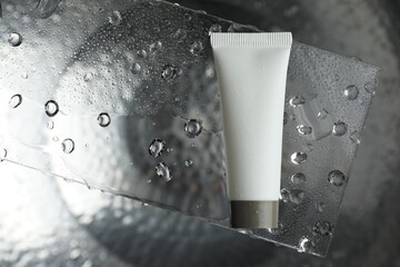 Moisturizing cream in tube on glass with water drops against metal background, top view. Space for...
