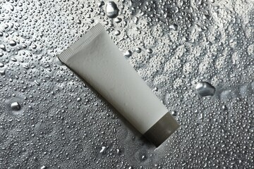 Moisturizing cream in tube on silver background with water drops, top view