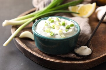Delicious yogurt in bowl, green onion, garlic and spoon on black table, closeup
