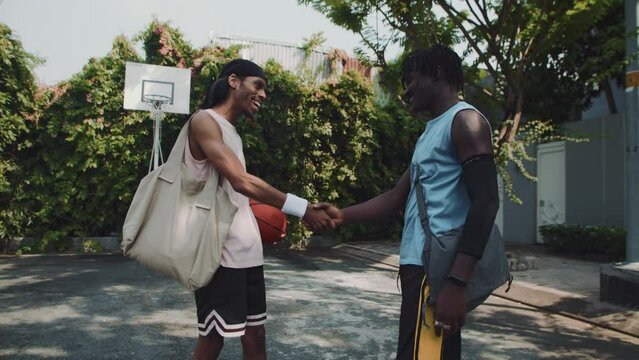 Medium long shot of two male friends shaking hands while meeting to play streetball outdoors