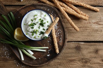 Delicious yogurt, green onion, grissini and lemon on wooden table, top view. Space for text