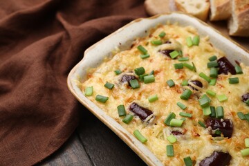 Tasty sausage casserole with green onions in baking dish on wooden table, closeup