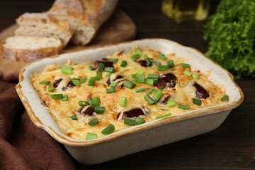 Tasty sausage casserole with green onions in baking dish on wooden table, closeup