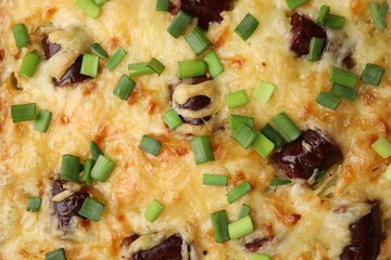 Tasty sausage casserole with green onions as background, top view