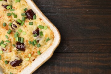 Tasty sausage casserole with green onions in baking dish on wooden table, top view. Space for text