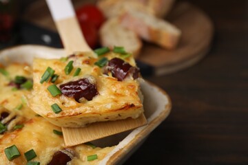 Taking piece of tasty sausage casserole from baking dish at table, closeup. Space for text